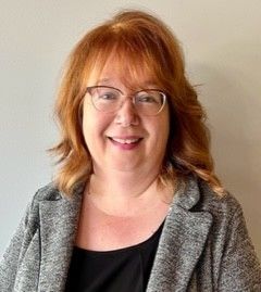 A woman with red hair and glasses smiling for the camera.